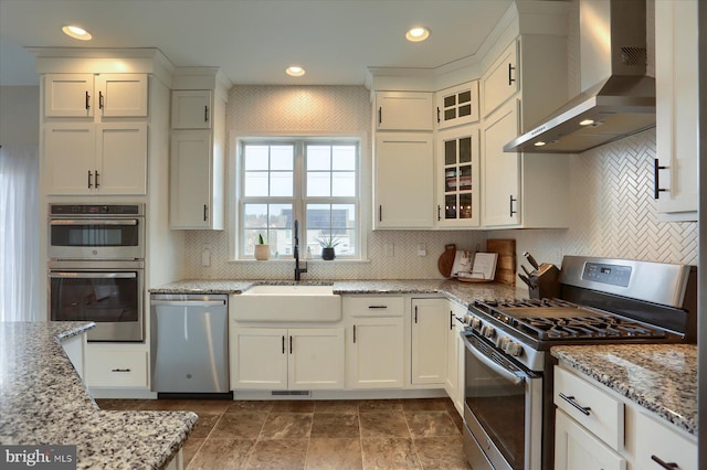 kitchen featuring sink, stainless steel appliances, light stone countertops, white cabinets, and wall chimney exhaust hood