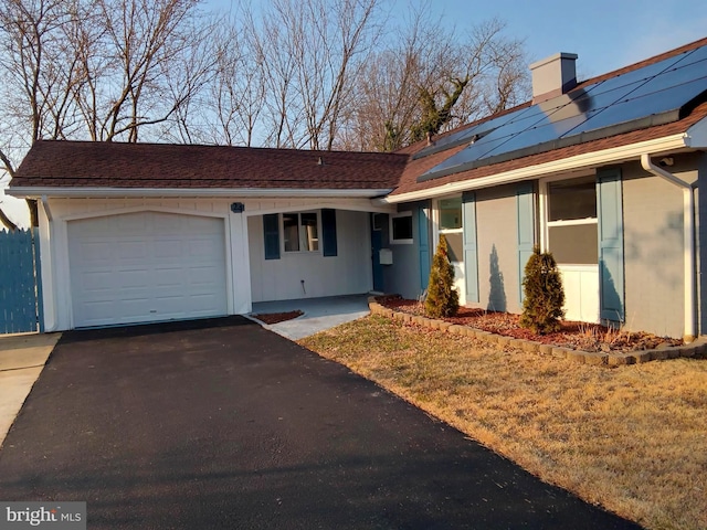 ranch-style house featuring aphalt driveway, a chimney, stucco siding, solar panels, and an attached garage