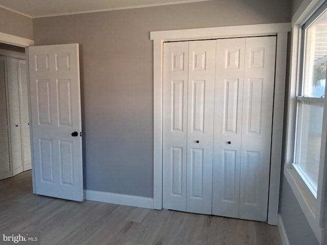 unfurnished bedroom featuring baseboards, crown molding, a closet, and light wood-style floors