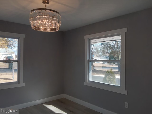 empty room featuring a chandelier, plenty of natural light, wood finished floors, and baseboards