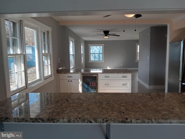 kitchen featuring stone counters, freestanding refrigerator, beverage cooler, and white cabinetry