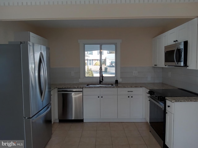 kitchen with tasteful backsplash, dark stone counters, stainless steel appliances, white cabinetry, and a sink