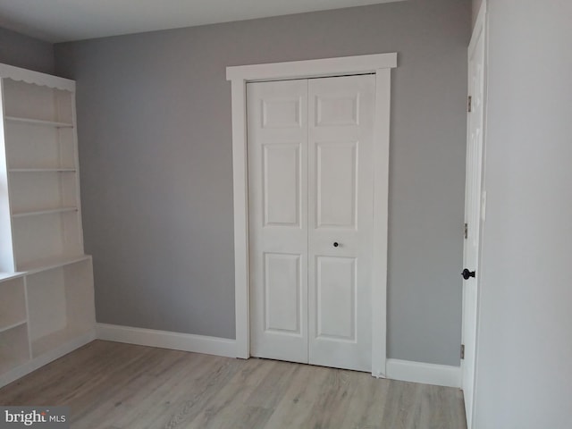 unfurnished bedroom with a closet, baseboards, and light wood finished floors