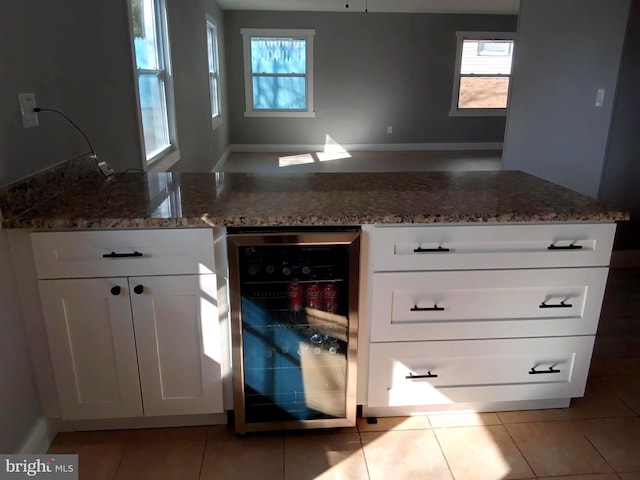 kitchen with dark stone counters, wine cooler, white cabinets, and light tile patterned floors