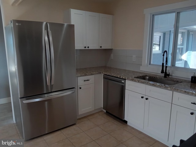 kitchen with light stone counters, stainless steel appliances, a sink, white cabinets, and decorative backsplash