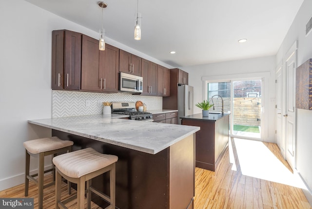 kitchen with appliances with stainless steel finishes, tasteful backsplash, a kitchen breakfast bar, kitchen peninsula, and light wood-type flooring