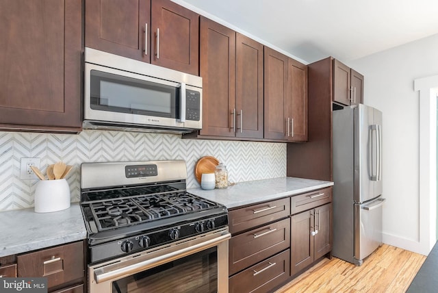 kitchen featuring stainless steel appliances, dark brown cabinetry, light stone countertops, decorative backsplash, and light wood-type flooring