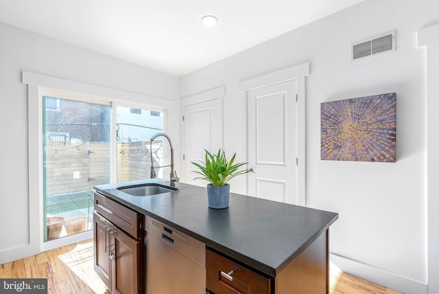 kitchen with white dishwasher, a kitchen island with sink, sink, and light wood-type flooring