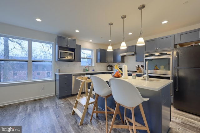 kitchen with sink, hardwood / wood-style flooring, appliances with stainless steel finishes, pendant lighting, and a kitchen island with sink