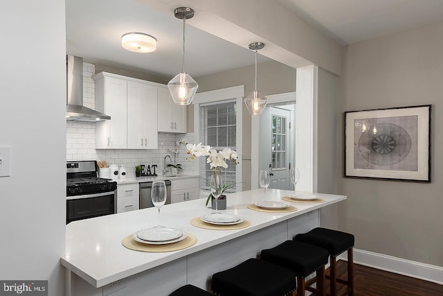 kitchen with wall chimney exhaust hood, a breakfast bar, stainless steel gas range, light countertops, and white cabinetry