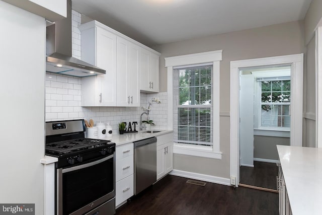 kitchen with light countertops, appliances with stainless steel finishes, wall chimney range hood, and white cabinets