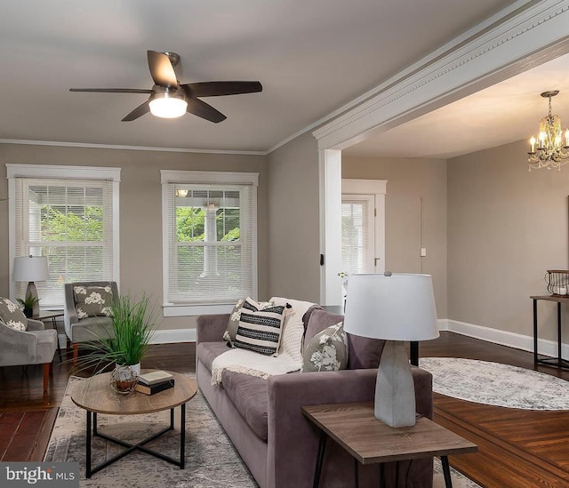 living room with baseboards, ornamental molding, wood finished floors, and ceiling fan with notable chandelier