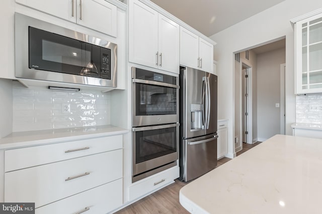 kitchen with white cabinetry, stainless steel appliances, light stone counters, and decorative backsplash