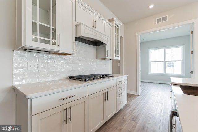 kitchen with stainless steel gas stovetop, white cabinets, decorative backsplash, custom range hood, and light wood-type flooring