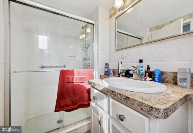 bathroom with backsplash, tile walls, vanity, and a shower with door