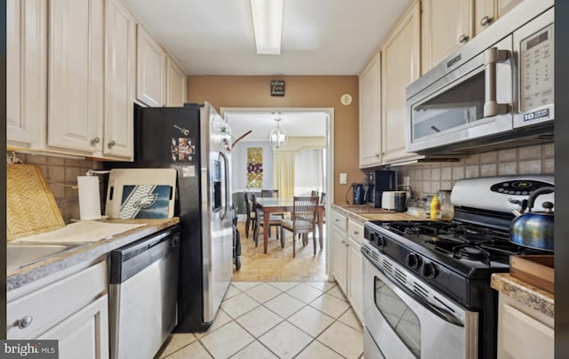 kitchen featuring appliances with stainless steel finishes, sink, backsplash, light tile patterned floors, and decorative light fixtures