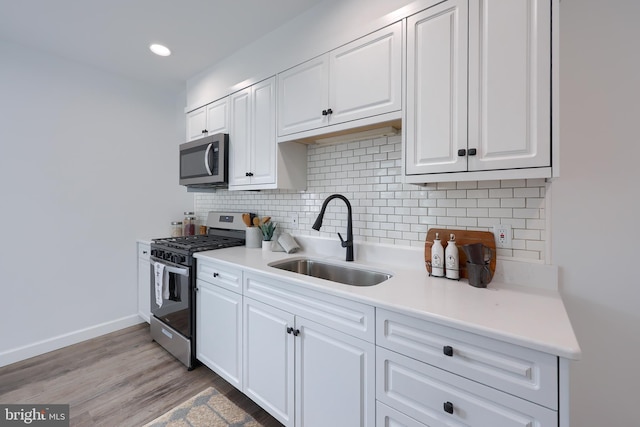 kitchen with appliances with stainless steel finishes, a sink, light countertops, white cabinetry, and backsplash