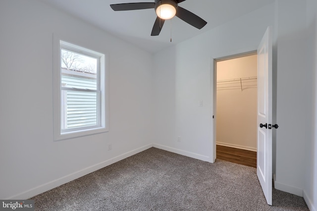 unfurnished bedroom with carpet floors, a closet, a spacious closet, a ceiling fan, and baseboards