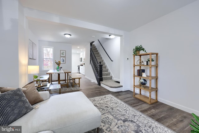 living area with stairs, baseboards, and dark wood-type flooring