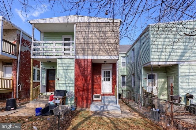 view of front facade with a balcony, fence, and brick siding