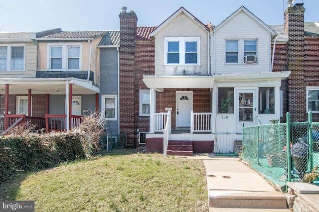 townhome / multi-family property featuring a porch, fence, a front yard, brick siding, and a chimney