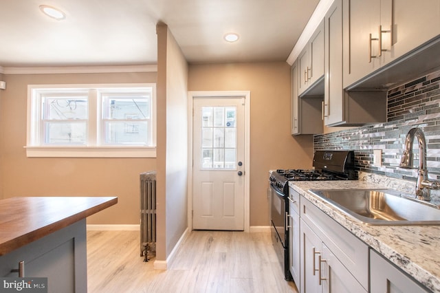 kitchen with radiator, black gas range oven, light wood finished floors, a sink, and decorative backsplash