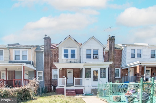 multi unit property with brick siding, a porch, a chimney, and fence