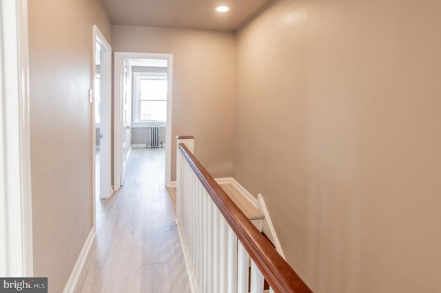 hallway with an upstairs landing, radiator, light wood-type flooring, and baseboards