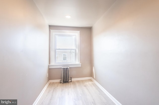 empty room featuring baseboards, light wood-style floors, and radiator heating unit