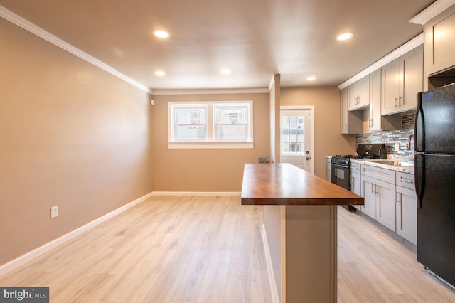 kitchen featuring gas range oven, decorative backsplash, light wood-style flooring, freestanding refrigerator, and wood counters