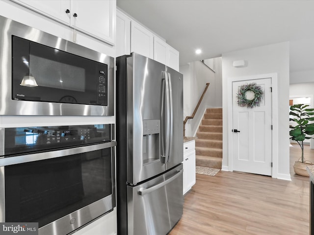 kitchen with stainless steel appliances, white cabinetry, light stone countertops, and light hardwood / wood-style floors