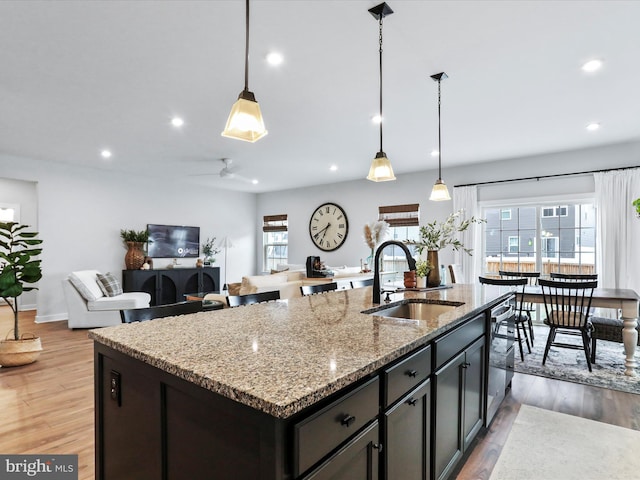 kitchen featuring sink, decorative light fixtures, a center island with sink, dishwasher, and light stone countertops