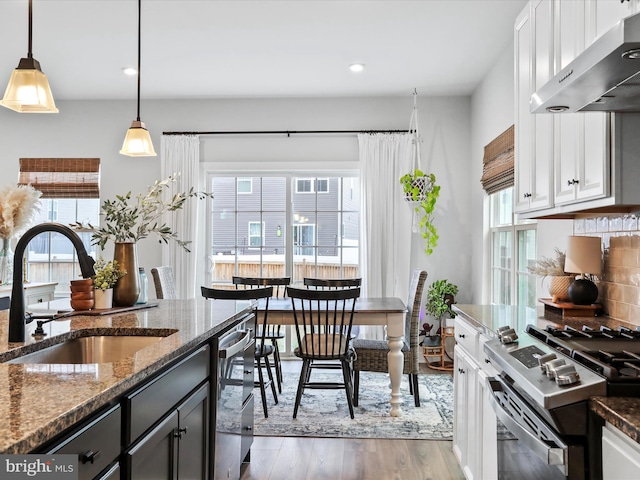 kitchen with sink, appliances with stainless steel finishes, white cabinetry, dark stone countertops, and decorative light fixtures