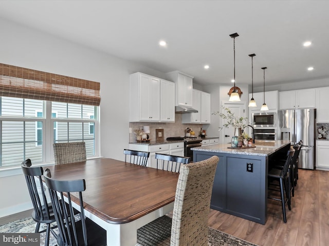 kitchen featuring a kitchen island with sink, decorative light fixtures, stainless steel appliances, and white cabinets