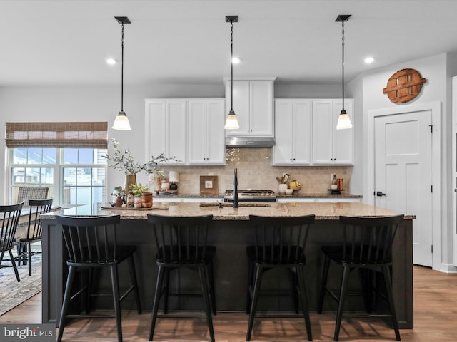 kitchen with a breakfast bar area, white cabinetry, backsplash, light stone counters, and an island with sink