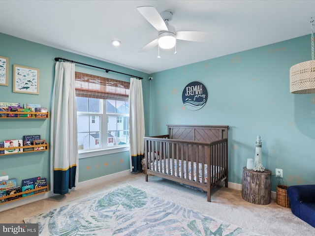 carpeted bedroom with a crib and ceiling fan