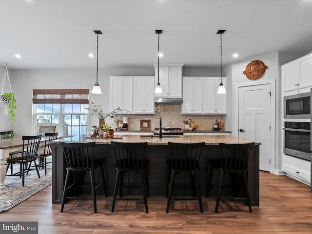 kitchen with stainless steel appliances, light stone countertops, a kitchen island with sink, and white cabinets