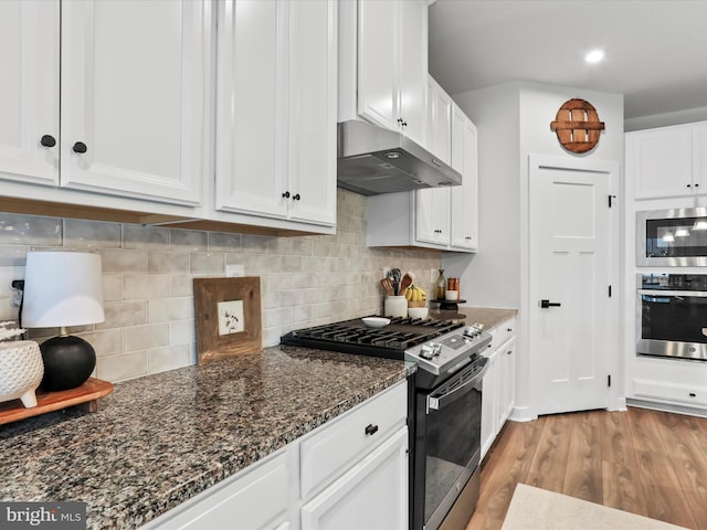 kitchen with appliances with stainless steel finishes, dark stone countertops, white cabinets, and light hardwood / wood-style flooring