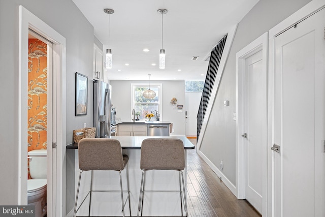 kitchen featuring appliances with stainless steel finishes, pendant lighting, white cabinetry, sink, and a kitchen breakfast bar