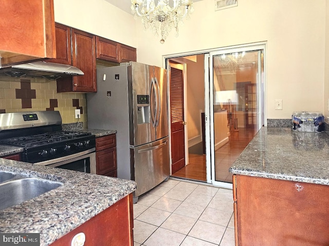 kitchen featuring tasteful backsplash, dark stone counters, light tile patterned floors, a notable chandelier, and stainless steel appliances