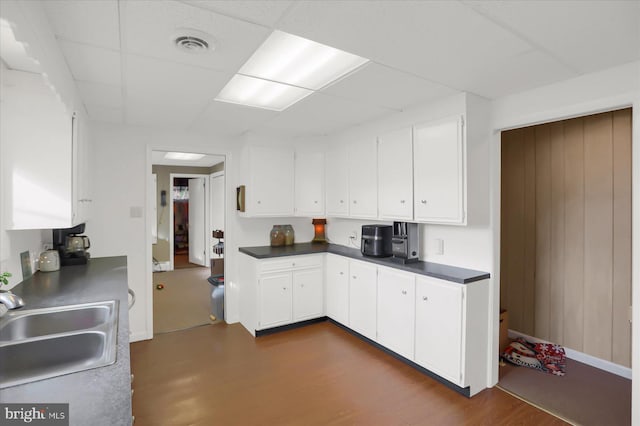 kitchen featuring sink, white cabinetry, wooden walls, a drop ceiling, and dark hardwood / wood-style flooring