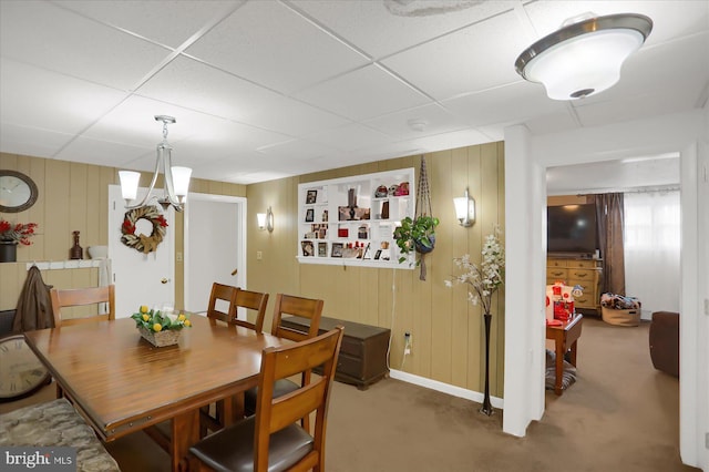 carpeted dining room with wood walls and a drop ceiling