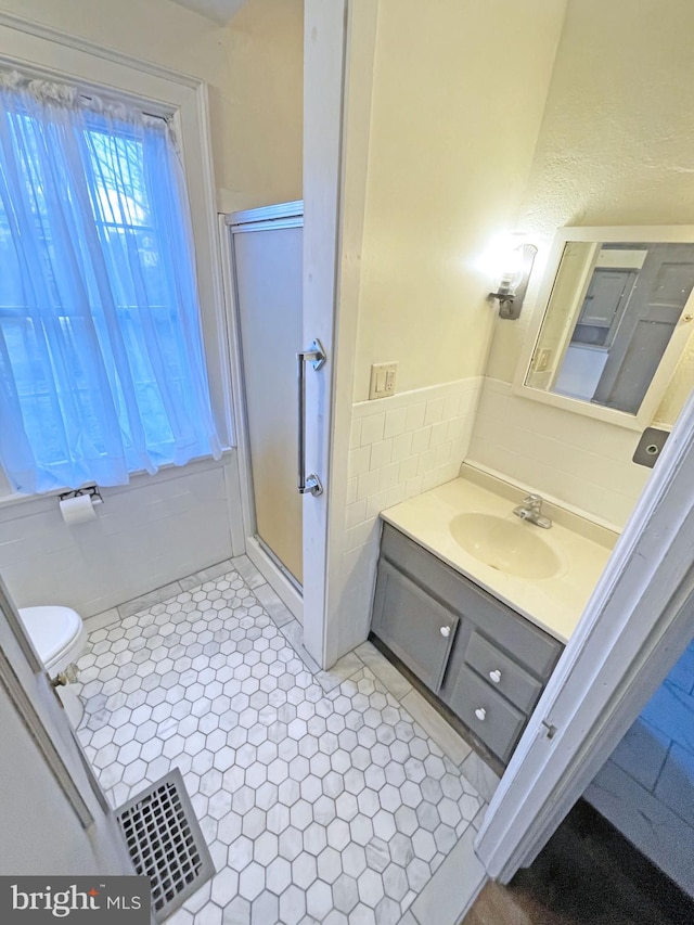 bathroom featuring tile walls, vanity, toilet, a shower with door, and tile patterned floors