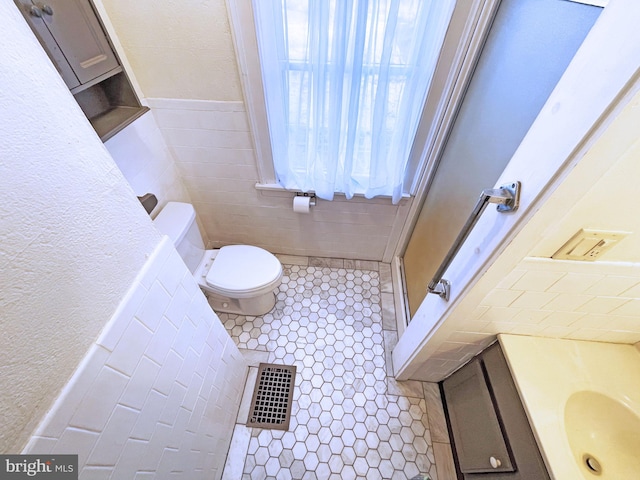 bathroom featuring sink, toilet, tile patterned flooring, and tile walls