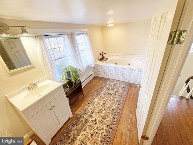 bathroom with wood-type flooring, a baseboard heating unit, tiled bath, and vanity