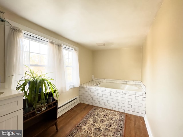 bathroom with tiled tub, a baseboard radiator, hardwood / wood-style floors, and vanity