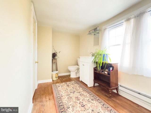 bathroom with wood-type flooring, a baseboard heating unit, and toilet