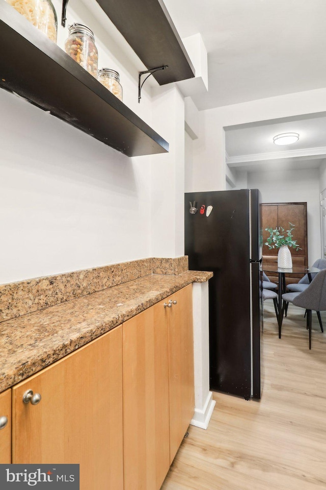 kitchen featuring light wood-type flooring, light stone countertops, and black fridge