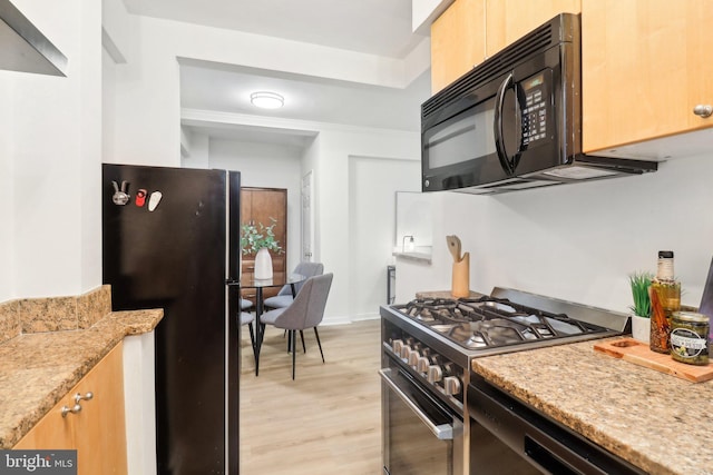 kitchen with light stone counters, light wood-type flooring, and black appliances