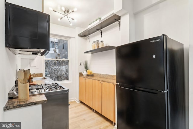 kitchen featuring black refrigerator, dark stone countertops, light hardwood / wood-style floors, gas range, and light brown cabinets